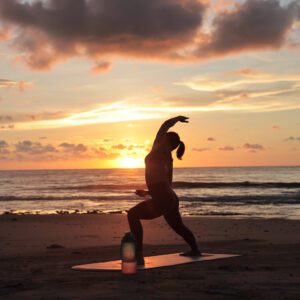 A woman doing yoga at a beach on a yoga mat